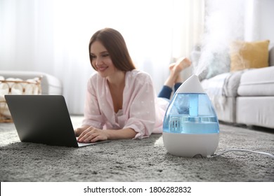 Woman with laptop near modern air humidifier at home
