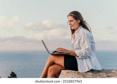 Woman Laptop Ocean View - Working remotely on clifftop overlooking sea at sunset. - Powered by Shutterstock