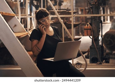 Woman, laptop and phone call or talk in factory, foundry and inventory for raw materials. Professional, quality control and browsing for service worker for machines, email and booking conversation - Powered by Shutterstock