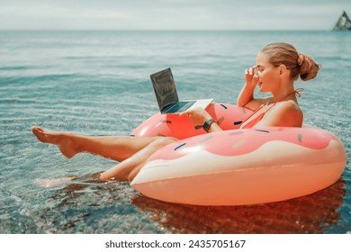 Woman laptop sea. Freelancer woman in sunglases floating on an inflatable big pink donut with a laptop in the sea. People summer vacation rest lifestyle concept - Powered by Shutterstock