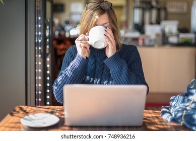 woman with laptop sipping large mug of latte at local coffee shop