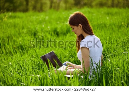 a woman with laptop sitting in a city park on the lawn on a hot summer day