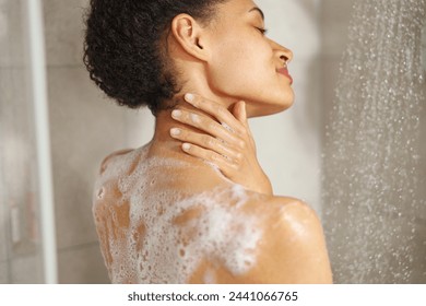 A woman lathers soap on her shoulder while taking a shower - Powered by Shutterstock