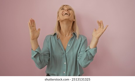 Woman laughing with joy, middle-aged, isolated, wearing a teal shirt against a pink wall background, happy and expressive, beautiful blonde female, youthful appearance. - Powered by Shutterstock