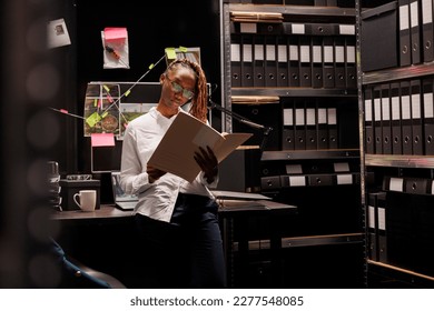 Woman law enforcement detective reading crime case document file in office. African american private investigator in glasses holding forensic expertise folder and studying conclusion - Powered by Shutterstock