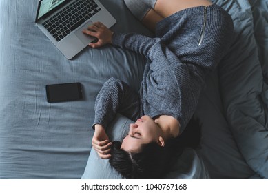 Woman Lay On Bed With Gray Sheets In Gray Clothes. Watch Movie On Laptop In Bed. Overhead View