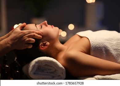 Woman lay on couch on her back with closed eyes and enjoy. Man make relaxing and therapeutic head massage at weight. Spa client has thrown her head back and rejuvenate. Wellness procedures in spa