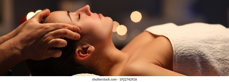 Woman lay on couch on her back with closed eyes and enjoy. Man make relaxing and therapeutic head massage at weight. Spa client has thrown her head back and rejuvenate. Wellness procedures in spa - Shutterstock ID 1922742926
