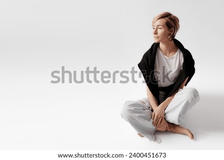 A woman in layered clothing sits thoughtfully, her casual chic style highlighted by a black sweater and light jeans