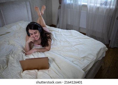 Woman Laying Down In Bed Working On Laptop Listening Music In Headset Bright White Room