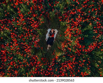 woman laying down on the middle of blooming poppies flowers field directly above