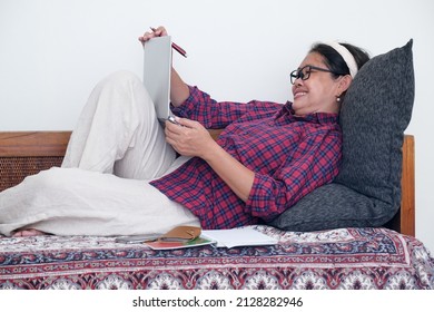 A Woman Laying Down, Smiling While Zooming; Smartphone And Agenda Next To Her.