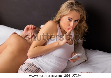Woman laying next to her boyfriend  holding her finger pressed against her lips 