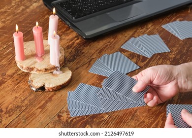 woman laying out cards for divination in front of a computer, candles, a laptop, playing cards on a wooden table, modern life and future predictions, fortune telling on the Internet - Shutterstock ID 2126497619