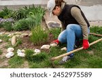 Woman laying out decorative stones on a flowerbed in the garden, country life concept