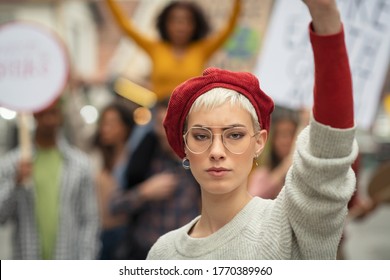 Woman leading a group of demonstrators on road for women rights. Young strong woman protest during a global strike. Portrait of angry girl in rally to protest on climate change looking at camera. 