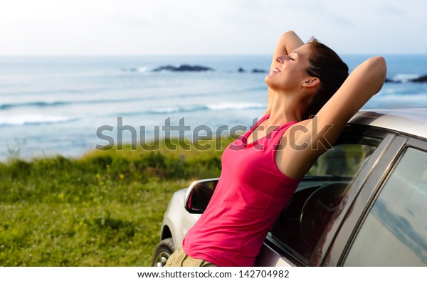 Woman\
leaning on car on summer travel to coast. Happy girl on road trip\
enjoying peace and silence relaxing on\
nature.