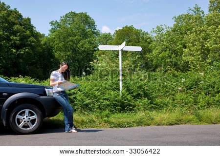 A woman leaning on her car as she reads a map next to a roadside sign, the sign is blank for you to add your own text.