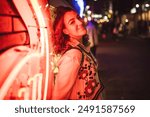 A woman leans against a neon-lit wall, smiling confidently in a vibrant night cityscape, capturing the lively energy and colorful atmosphere of urban nightlife.