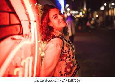 A woman leans against a neon-lit wall, smiling confidently in a vibrant night cityscape, capturing the lively energy and colorful atmosphere of urban nightlife. - Powered by Shutterstock