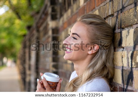 Woman leans against wall and enjoys a Cup of coffee