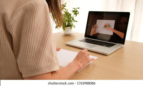 Woman learning to draw an online course online sitting at home looking over her shoulder  Drawing lesson online laptop works computer