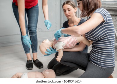 Woman learning how to make chest compressions on a baby dummy during the first aid group training indoors - Powered by Shutterstock