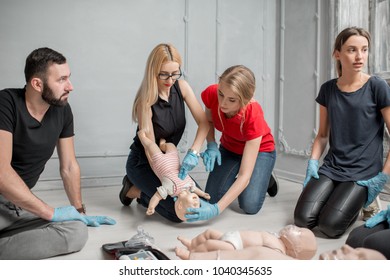 Woman learning how to make chest compressions on a baby dummy during the first aid group training indoors - Powered by Shutterstock