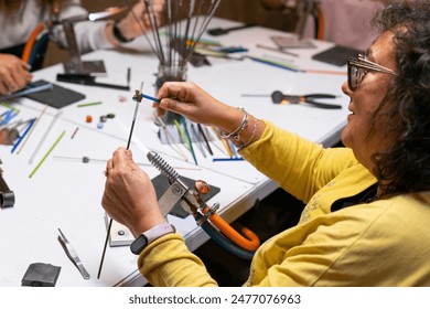 Woman learning to make handmade glass jewelry in a workshop - Powered by Shutterstock