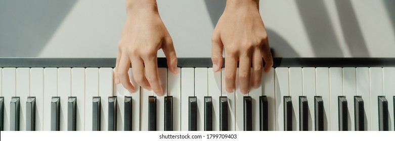 Woman learning to play piano at home on digital keyboard. Panoramic banner crop of hands playing beginner chords to learn playing by herself.
