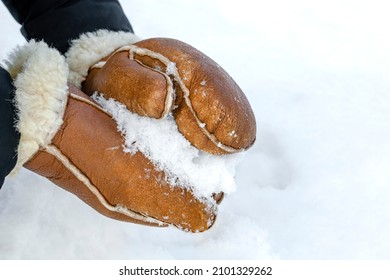 Woman in leather mittens rolls a snowball outdoors, close-up. Hands in warm mittens make snow in winter. Brown leather mittens in the snow in winter.