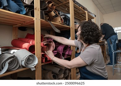 Woman leatherworker selects a roll of leather in the workshop.  - Powered by Shutterstock