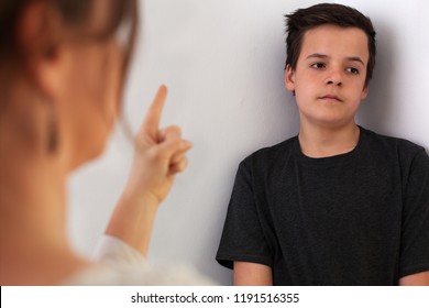 Woman lecturing her teenager son pointing with finger to a boy with bored expression, adolescence problems concept