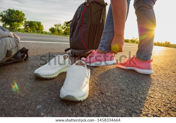 The woman left the work shoes and wore sneakers on
the highway with the golden light of the sun. Concept of vacation
and travel
