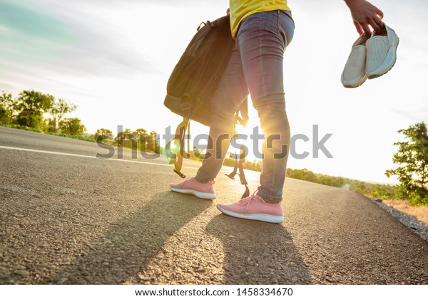 The woman left the work shoes and wore sneakers on\
the highway with the golden light of the sun. Concept of vacation\
and travel