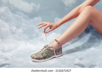 Woman leg with anklet in stylish lumina sage sneaker isolated on blue cloud sky background, space for text