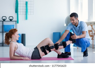 Woman with leg injury on mat and smiling doctor during treatment in the hospital
