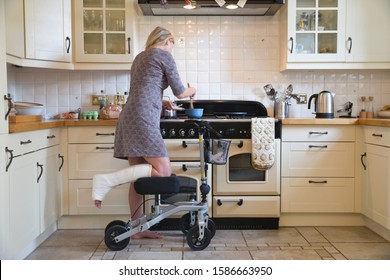 Woman With Leg In Plaster Cast At Home Using Mobility Aid Whilst Cooking Meal