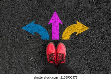 woman legs in boots standing on road with three direction arrow choices, left, right or move forward  - Shutterstock ID 2138900375