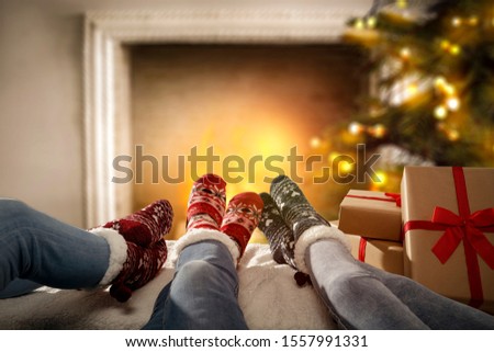 Woman legs with christmas socks and fireplace with xmas tree in home interior.