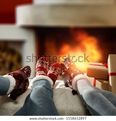 Woman legs with christms woolen socks and free space for your decoration. Home interior with fireplace and warm orange color of fire.Copy space and december xmas time. 