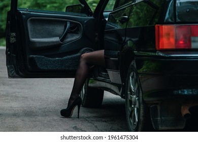 Woman Legs In High Heel Shoes Stick Out Of The Car. Sexy Girl Gets Out Of The Car. Girl In Pantyhose And Black Shoes. Vintage-effect Photography And Film Grain