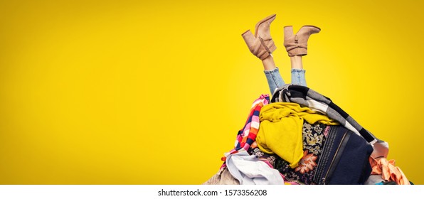 woman legs out of clothes pile on yellow background with copy space - Shutterstock ID 1573356208