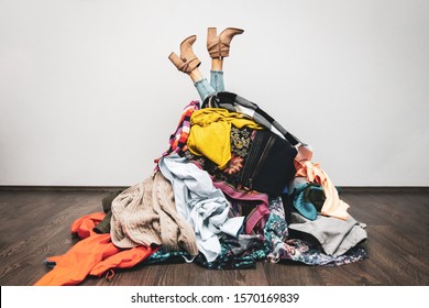 Frauenbeine aus einem Kleider-Haufen auf dem Boden. Einkaufsdrosselkonzept