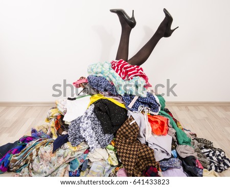 Woman legs reaching out from a big pile of clothes and accessories. Woman buried under an untidy cluttered woman wardrobe. Woman in high heels needs help from to much shopping. Shopaholic girl.