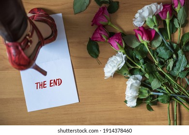 Woman legs in red high heel shoes walking on paper with word the end on a floor with withered flowers. Heart broken concept. Divorce 