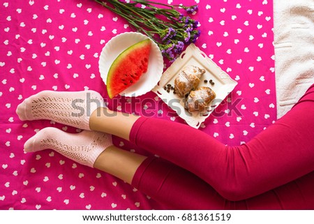 Woman legs with red pants lying on pink blanket with breakfast in bed