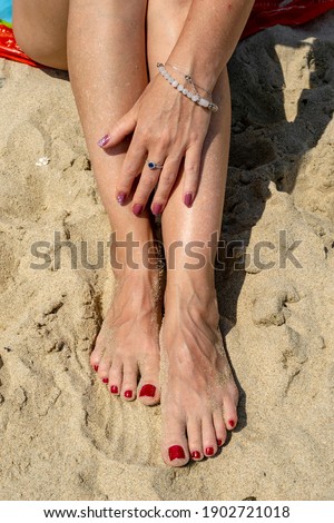 Woman legs with red pedicure relaxing on the sand. The hand strokes the leg. Summer beach.