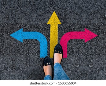 woman legs in shoes standing on road with three direction arrow choices, left, right or move forward - Shutterstock ID 1580055034