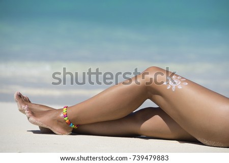 Woman legs with sun-shaped sun cream in the tropical beach conceptual image of vacation